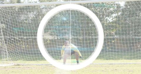 Crouching goalkeeper guarding soccer goal wearing yellow jersey and gloves with lens flare