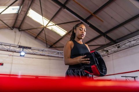 Female boxer preparing with focus pad in ring training gym showing concentration and determination