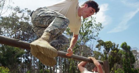 Determined soldiers overcoming obstacle course hurdle outdoors