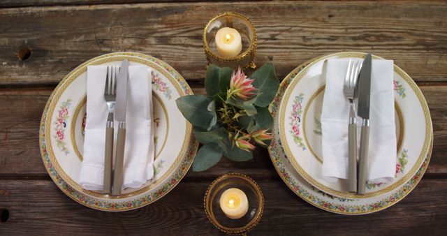 A romantic dinner setting for two with vintage plates, lit candles, and a floral centerpiece on a rustic wooden table. The ambiance suggests an intimate and cozy dining experience, perfect for a couple's evening.