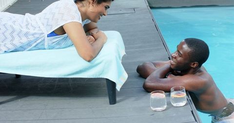 Couple enjoying sunny poolside conversation with refreshing citrus water on deck