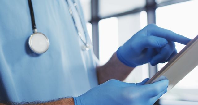 Caucasian male doctor wearing protective gloves using digital tablet. medical professional healthcare worker hygiene during coronavirus covid 19 pandemic.