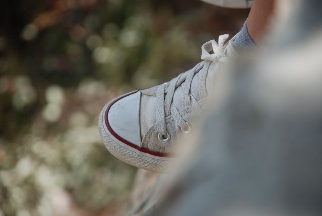 Focus on white canvas sneaker with laces, blurred natural background. Perfect for fashion blogs, casual wear promotions, shoe stores, and outdoor activity advertisements.