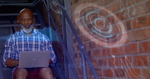 Senior man using laptop with holographic hud overlay on industrial stairs in urban loft