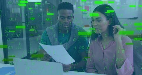 Coworkers reviewing documents on laptop with binary code overlay, collaborating on data