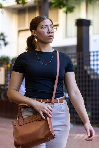 African american woman walking sidewalk wearing black top carrying tan leather handbag