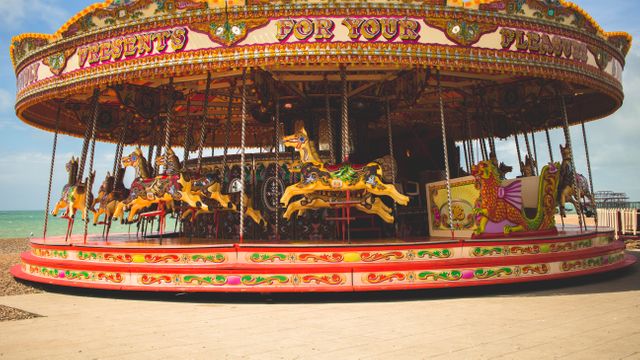 A brightly colored, vintage-style carousel at a seaside amusement park featuring elaborately decorated horses. Ideal for use in vacation brochures, advertisements for amusement parks, websites promoting family destinations, or nostalgic-retro themed projects.