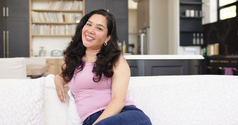 Smiling woman relaxing on white sofa in modern open-plan living room with kitchen backdrop