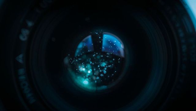 Macro camera lens glass revealing teal bokeh, water droplets, aperture glints and optical texture