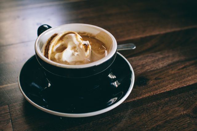 Close-up of steaming espresso served in a black cup with creamer, placed on a wooden table. This image is perfect for promoting cafes, coffee shops, or beverage-related blogs. It evokes a warm, inviting atmosphere ideal for marketing, advertisement, or social media posts focused on relaxation, coffee culture, and morning rituals.