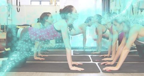 Women holding plank in group pilates class on black mats in sunlit gym mirror reflection