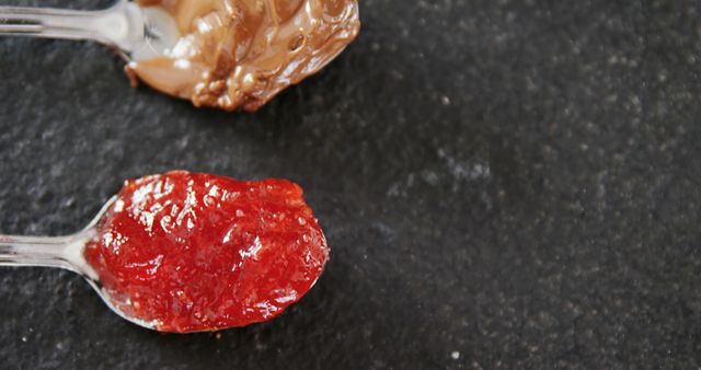 This image shows a close-up of two plastic spoons, one holding jam and the other holding nut butter, placed on a dark surface. Useful for food blogs, recipe websites, and advertisements featuring spreads or snacks.