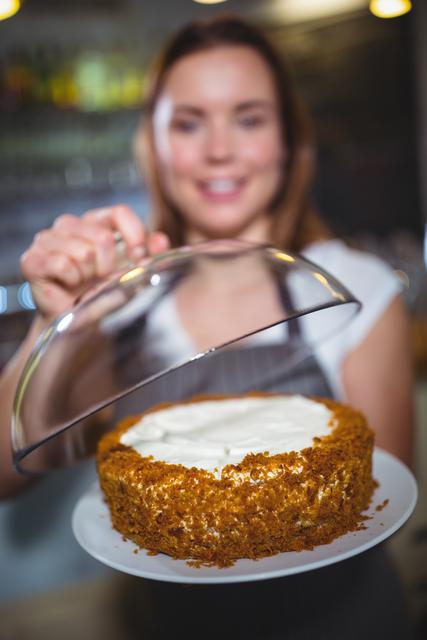 Waitress in a cafe holding a freshly baked cake with a smile. Ideal for use in advertisements for cafes, bakeries, or restaurants. Can also be used in articles or blogs about hospitality, food service, or baking. Perfect for promoting desserts and sweet treats.