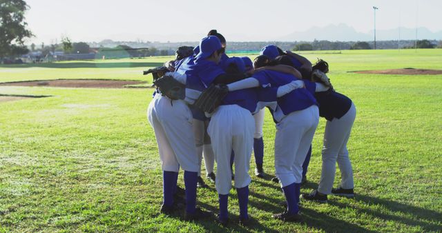 Youth baseball team huddling on a grassy field, creating a unified circle. Players wearing baseball uniforms, showing teamwork and strategy preparation before a game. Useful for content related to youth sports, teamwork, outdoor activities, and athletic training.