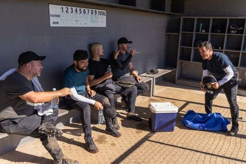Baseball teammates relaxing in dugout drinking water and laughing during sunny game break