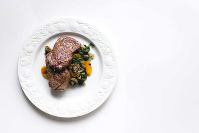 Elegant presentation of cooked steak served with sautéed vegetables on elegant plate. Ideal for use in culinary blogs, restaurant menus, healthy eating promotions, or food advertisements.