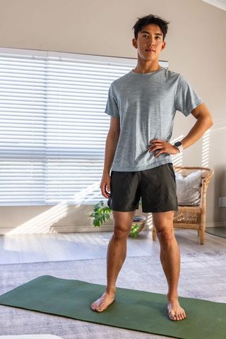Asian man standing on green yoga mat checking smartwatch during home workout routine
