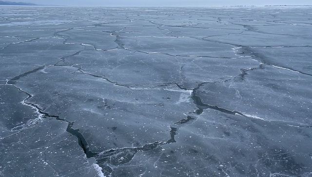 Frozen lake cracking into polygonal ice floes revealing narrow leads under overcast sky