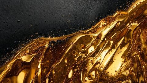 Flowing liquid gold creating glossy ribbons, droplets and micro-splatter on matte black