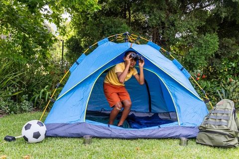 Backyard camping adventure with african american child peering through binoculars in tent
