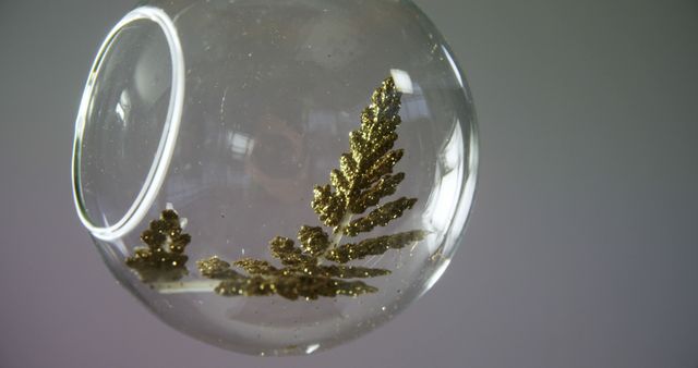 Close-up view of a transparent spherical glass ornament featuring a delicate golden fern design. Ideal for use in holiday decor displays, craft projects, and promoting handmade arts. Suitable for nature enthusiasts and to add an artistic touch to home decor themes.