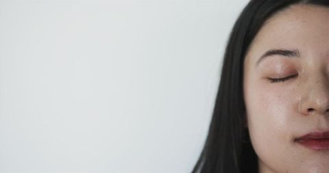 Young woman closing eyes and relaxing in soft light with minimal neutral background