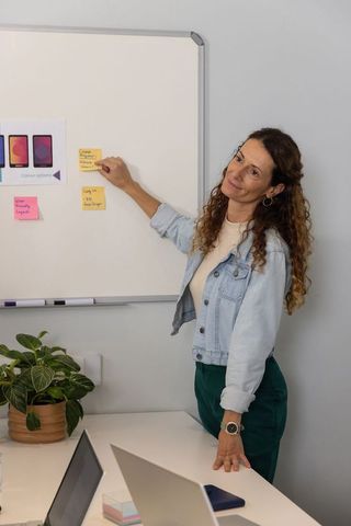 Mature woman leading collaborative planning session with sticky notes on whiteboard