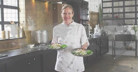 Female chef presenting plated salads in industrial kitchen with world map overlay