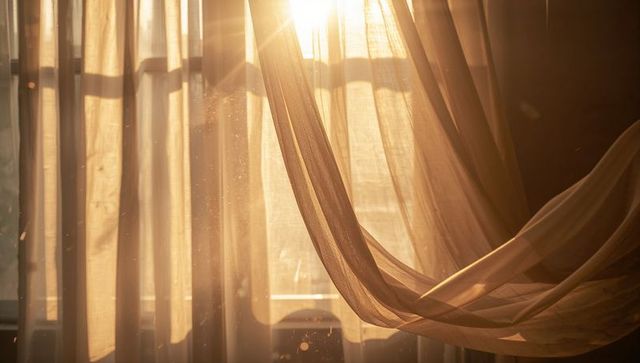 Sunlit sheer curtain flowing across window, casting dust motes and warm golden glow