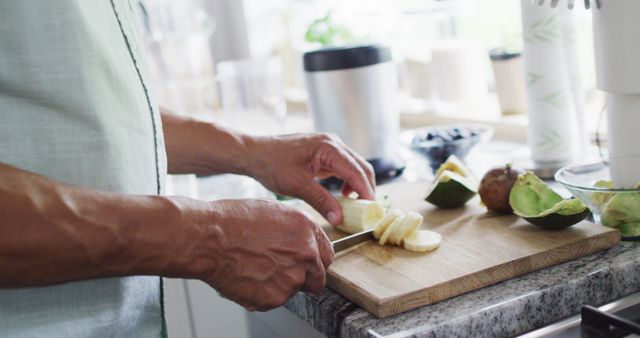 Person slicing an avocado on wooden cutting board in a bright, modern kitchen. Image can be used for topics related to healthy eating, meal preparation, cooking tutorials, diet and wellness blogs, or kitchen appliances promotions.