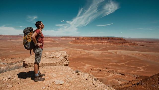 Standing hiker overlooking vast desert canyon and layered mesa with backpack and solitude