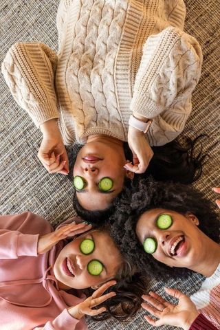 Diverse friends enjoying cozy at-home spa day with cucumber slices and knitwear