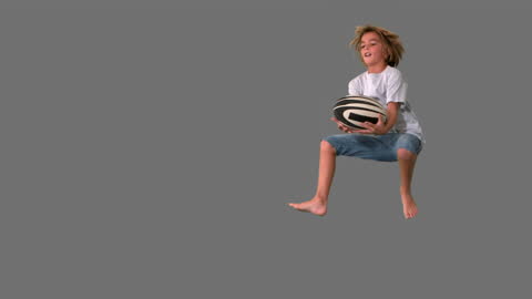 Joyful Boy Jumping to Catch Rugby Ball with Grey Background