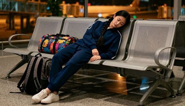 Sleeping traveler on airport bench with floral duffel and backpack at night terminal