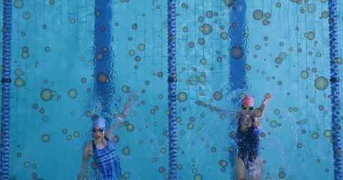 Overhead: two female competitive swimmers training in pool lanes with bubbles and goggles