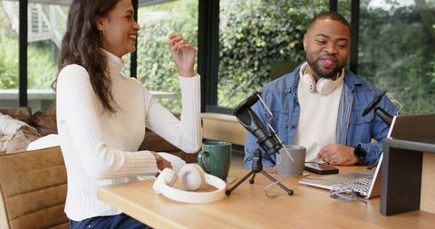 Recording conversational podcast with diverse co-hosts at cozy home studio table, natural light