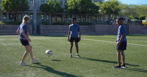 Multiracial teens kicking soccer ball on school turf practicing teamwork and fitness