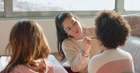 Friends applying makeup in sunlit living room during cozy at-home beauty session