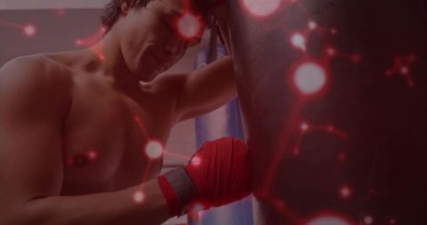 Shirtless male boxer training with red hand wraps hitting heavy bag, focused athlete