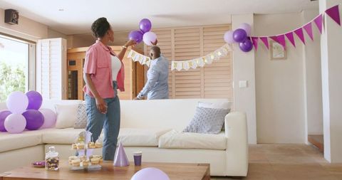 African American couple decorating living room with purple balloons and birthday banner