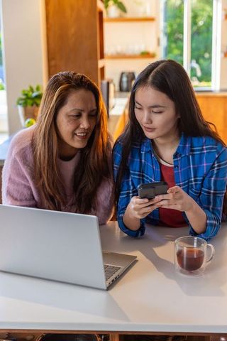 Mother and Daughter Connecting Digital Devices in Cozy Kitchen