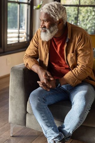 Contemplative senior african american man sitting by window wearing smartwatch, sunlit interior