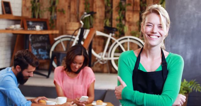 A cheerful barista smilings inside a cozy coffee shop. In the background, two customers sit with drinks, chatting and enjoying their time. The wooden walls and bicycle artwork create a warm and inviting atmosphere. Ideal for marketing coffee shops, hospitality, customer service, or promoting friendly business environments.