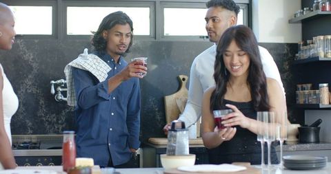 Multicultural friends gathering at kitchen island pouring drinks smiling asian woman
