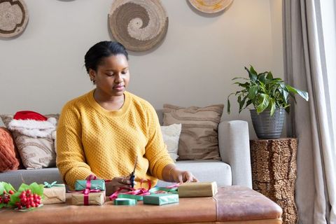 African american woman wrapping holiday gifts on ottoman in cozy living room with natural light