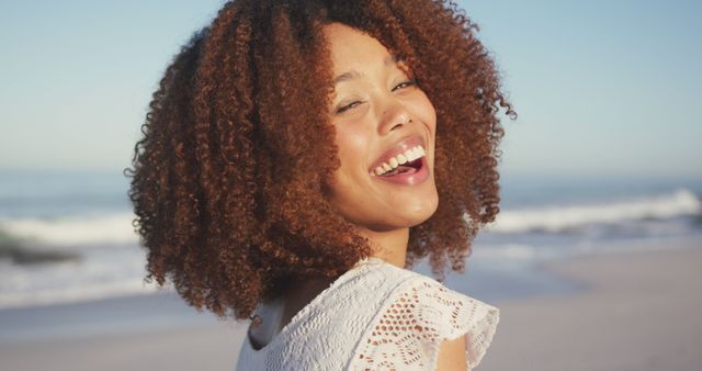Vibrant and carefree African American woman enjoying time at the beach on a sunny day. Perfect for promoting tourism, lifestyle blogs, fashion, beauty products, and mental wellness. Use in campaigns focusing on happiness, summer adventures, and freedom.