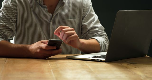 Man Using Smartphone While Working on Laptop at Wooden Desk - Download Free Stock Images Pikwizard.com