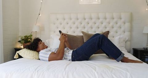 Relaxed Man with Smartphone on Modern Bed in Cozy Bedroom