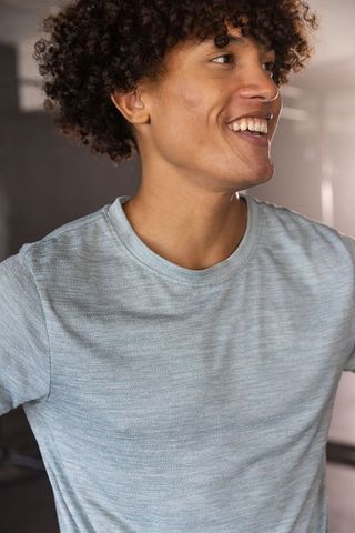 Curly-haired person smiling in light grey t-shirt with natural light
