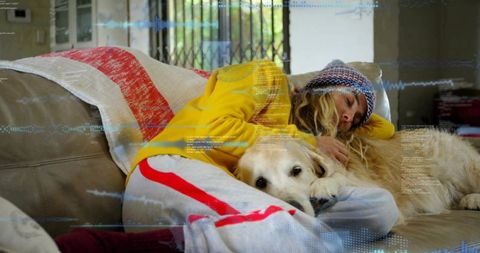 Young woman napping on couch cuddling golden retriever under cozy blanket with beanie